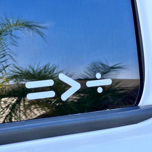 May include: A white vinyl sticker with the text "=> :" on a black car window.