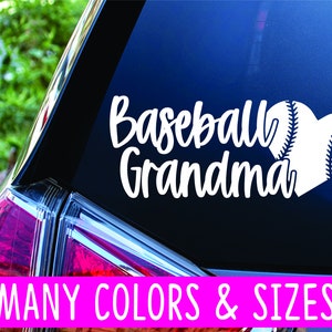 May include: White vinyl decal with the text "Baseball Grandma" and a white baseball heart. The decal is on the back window of a car. The text "MANY COLORS & SIZES" is on a pink banner at the bottom of the image.