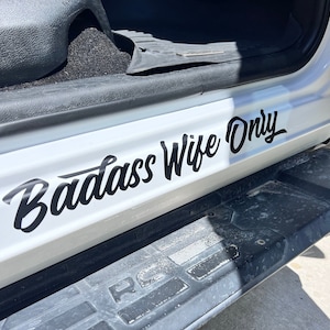 May include: A white vehicle door with a black vinyl decal that reads "Badass Wife Only".