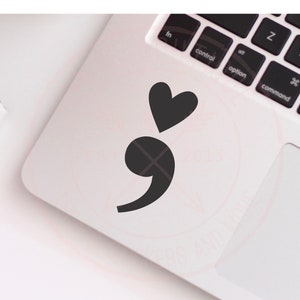 May include: A black semicolon and heart sticker on a white laptop.