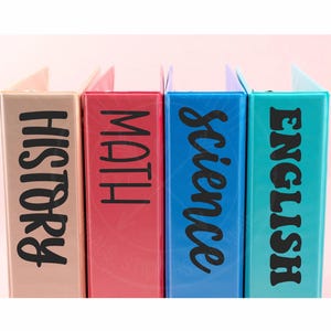 May include: Four three-ring binders in light pink, dark pink, blue, and teal. Each binder features black lettering on the spine reading HISTORY, MATH, SCIENCE, and ENGLISH respectively. The binders are arranged side-by-side in a vertical row.