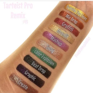 May include: A close-up of an arm displaying eyeshadow swatches from the Tarteist Pro Remix collection. The swatches include shades like "Create," "Graphic," "Beat Drop," "Color Explosion," "Sway," "Mashup," "Moonlit," "Graffiti," "Mic Drop," and "Outside The Lines."