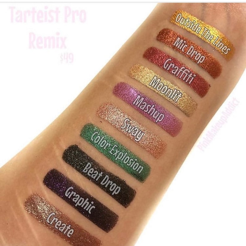 May include: A close-up of an arm displaying eyeshadow swatches from the Tarteist Pro Remix collection. The swatches include shades like "Create," "Graphic," "Beat Drop," "Color Explosion," "Sway," "Mashup," "Moonlit," "Graffiti," "Mic Drop," and "Outside The Lines."