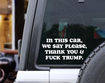 Könnte beinhalten: Weißer Vinyl-Autoaufkleber mit dem Text "IN THIS CAR, we say PLEASE, THANK YOU & FUCK TRUMP." Der Aufkleber ist auf einer Autoscheibe angebracht. Das Auto ist weiß und der Reifen ist sichtbar.