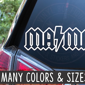May include: White vinyl decal with the text "me/me" in a bold, gothic font style. The text is on a black background. The decal is on the back window of a car.