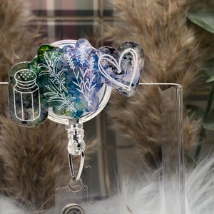 May include: A clear badge reel with a white heart, a salt shaker, and a sprig of greenery on a colorful background.