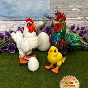 May include: A white chicken, a green and red rooster, and a yellow chick stand on a green surface with white eggs. The rooster has a red comb and wattle. The chick has a yellow beak and orange legs. The background is a light blue and gray wooden surface with purple flowers.