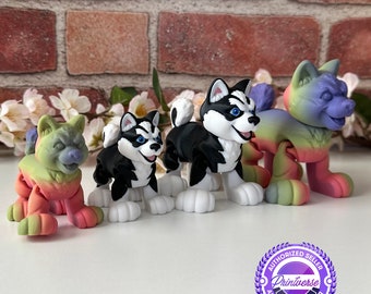 May include: Four colorful husky dog figurines. Two are black and white, one is rainbow-colored, and one is green and pink. The figurines have white paws and are posed in a playful stance. The background includes a brick wall and white flowers.