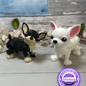 Puede incluir: Dos figuritas de chihuahua impresas en 3D, una negra y otra blanca, con orejas rosas. Las figuritas están de pie sobre una superficie de madera con una pegatina púrpura y blanca que dice "Vendedor autorizado Printverse Vendedor autorizado".