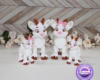 May include: A set of four white fondant goat figurines. The goats are different sizes and have brown hooves and pink bows. The largest goat has a pink bow on its head. The figurines are on a white surface with a wooden background.