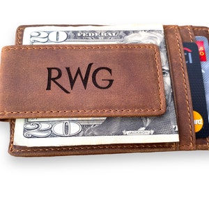 May include: A brown leather wallet with a money clip and a card slot. The wallet has the initials "RWG" engraved on the front.