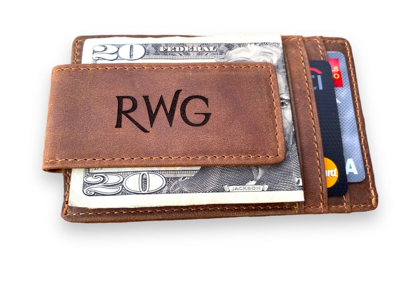 May include: A brown leather wallet with a money clip and a card slot. The wallet has the initials "RWG" engraved on the front.