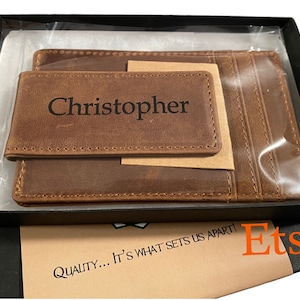May include: A brown leather wallet with a money clip and a card slot. The wallet is personalized with the name "Christopher".