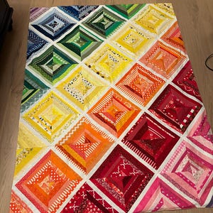 May include: A rainbow quilt with a diamond pattern. The quilt is made of various fabrics in shades of blue, green, yellow, orange, red, and pink.