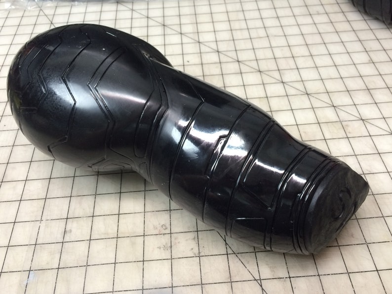May include: Black plastic arm piece with a textured, geometric design. The piece is curved and has a rounded end.