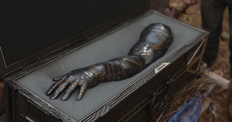 May include: A black and gold robotic arm is displayed in a wooden box with a gray lining. The arm is fully extended and the hand is open.