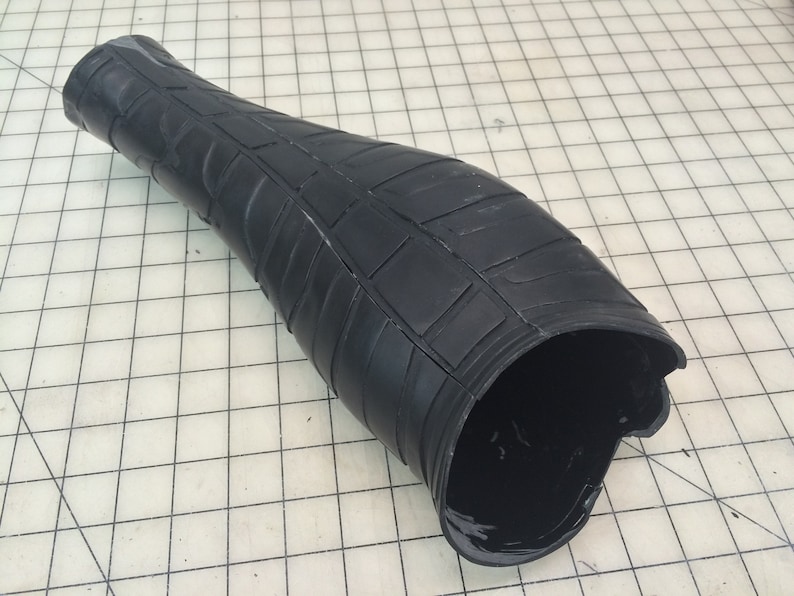 May include: Black rubber forearm armor with a textured surface. The armor is designed to resemble a segmented, articulated piece of protective gear.