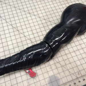 May include: A black plastic arm with a segmented design. The arm is articulated at the elbow and has a textured surface.