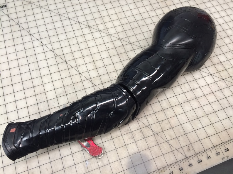 May include: A black plastic arm with a segmented design. The arm is articulated at the elbow and has a textured surface.