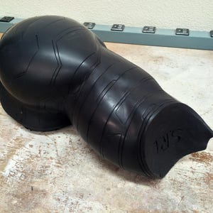 May include: Black rubber mold of a human arm, with a textured surface and the letters "J.S." on the back.
