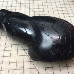 May include: Black rubber arm guard with a textured, geometric pattern. The guard is designed to protect the arm from impact.