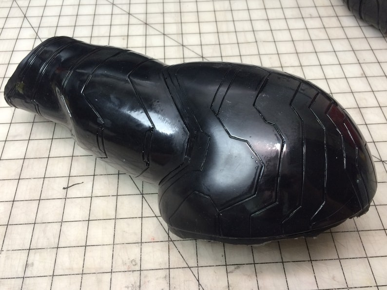 May include: Black rubber arm guard with a textured, geometric pattern. The guard is designed to protect the arm from impact.