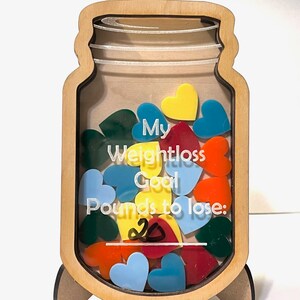 May include: Wooden jar-shaped weight loss goal tracker with a clear acrylic window. The jar is filled with colorful heart-shaped pieces. The text on the jar reads "My Weightloss Goal Pounds to lose: 20".