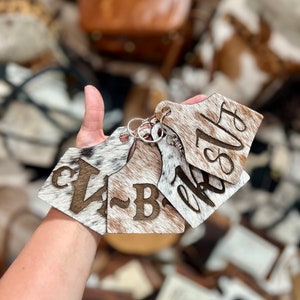 May include: Three cowhide keychains with the letters "VB" and "6815" engraved on them. The keychains are attached to a silver key ring.