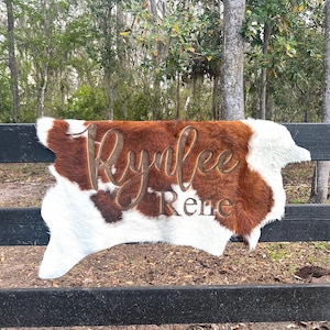 Może przedstawiać: Dywan ze skóry krowiej z wyciętymi nazwami "Rynlee Rene" w brązowym futrze.