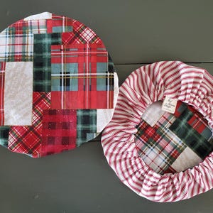 May include: Two round fabric bowl covers. One is a patchwork of red, green, and white plaid fabrics. The other has a red and white striped exterior and a plaid interior. The covers are designed to fit over bowls.