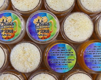 Może przedstawiać: Wiele małych, przezroczystych plastikowych słoiczków wypełnionych jasnożółtym peelingiem do ust. Każdy słoiczek ma etykietę z napisem "Artisan Bath Co. LIP SCRUB ButterBeer 0.5 OZ - 14g". Peeling ma ziarnistą konsystencję i złote płatki.