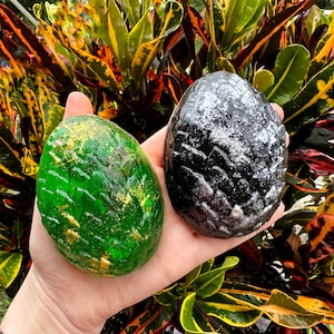 Peut inclure: Deux savons en forme d'&oelig;uf de dragon, l'un vert avec des paillettes dor&eacute;es et l'autre noir avec des paillettes argent&eacute;es.