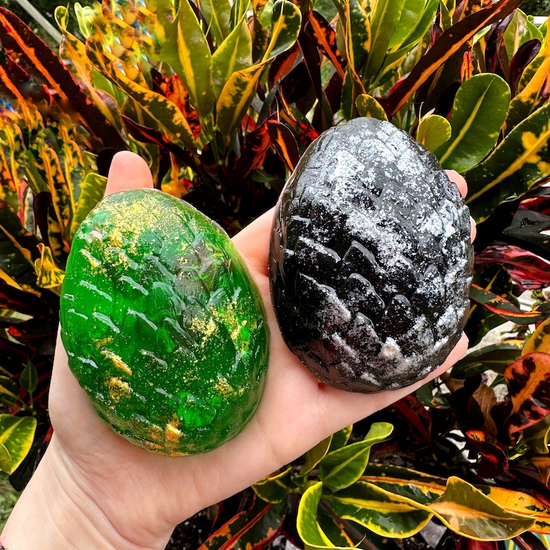 Peut inclure: Deux savons en forme d'&oelig;uf de dragon, l'un vert avec des paillettes dor&eacute;es et l'autre noir avec des paillettes argent&eacute;es.