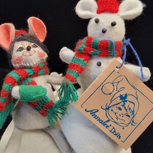 Puede incluir: Dos mu&ntilde;ecos de rat&oacute;n de peluche, uno gris y otro blanco, con bufandas y sombreros rojos y verdes. El rat&oacute;n blanco tiene un sombrero rojo con un pomp&oacute;n verde. El rat&oacute;n gris tiene un sombrero negro. Una etiqueta dice "Annalee Dolls".