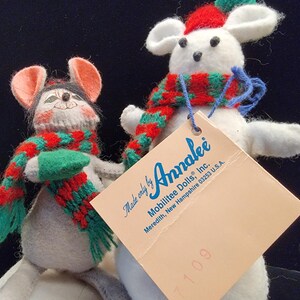 Puede incluir: Dos mu&ntilde;ecos de rat&oacute;n de fieltro, uno gris y otro blanco, con bufandas y sombreros rojos y verdes. Los mu&ntilde;ecos tienen ojos de bot&oacute;n negros y se dan la mano. Una etiqueta de Annalee Dolls est&aacute; adjunta al rat&oacute;n blanco.