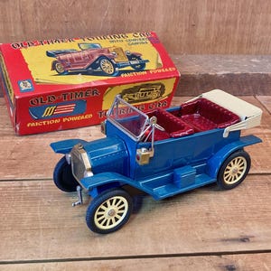 Pode incluir: Carro de brinquedo azul e branco com bancos vermelhos e capota de lona branca. O carro é etiquetado como "Old-Timer Touring Car" e "Friction Powered".