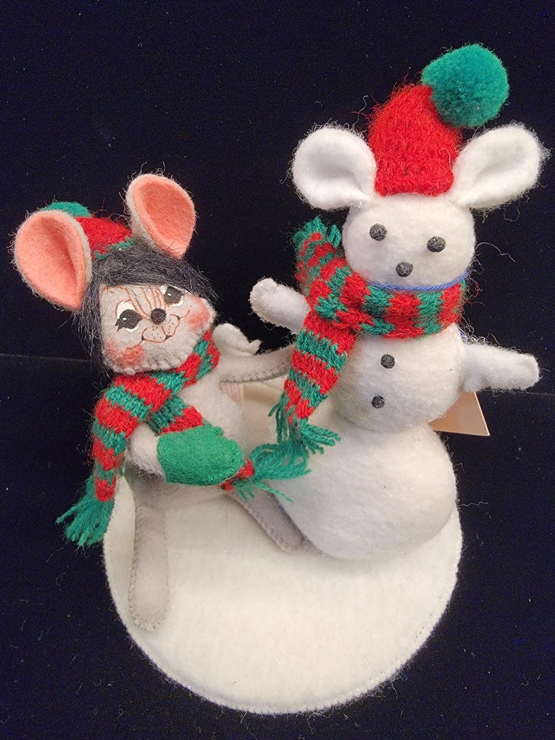 Puede incluir: Dos ratones navide&ntilde;os de fieltro, uno montado en un mu&ntilde;eco de nieve. Los ratones llevan bufandas y gorros a rayas rojas y verdes. El mu&ntilde;eco de nieve es blanco con ojos de bot&oacute;n negros y una nariz de zanahoria. La base es un c&iacute;rculo de fieltro blanco.