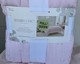 Może przedstawiać: Różowy koc w rozmiarze Full/Queen z kwiatowym wzorem. Koc jest owinięty białą taśmą i posiada logo marki "Shabby Chic". Koc ma wymiary 229cm x 229cm.