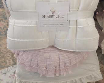 Może przedstawiać: Biały zestaw kołdry Shabby Chic, złożony i zabezpieczony białą opaską. Zestaw zawiera kołdrę i poduszkę, spoczywające na krześle z różową koronkową osłoną. Poduszka ma niebieski kwiatowy wzór.
