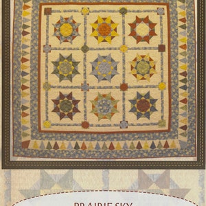 Op de afbeelding: Een quiltpatroon genaamd "Prairie Sky" met een patchwork-ontwerp met een raster van negenpuntige sterren in tinten bruin, geel en blauw. Het patroon wordt omringd door een rand van driehoeken in tinten blauw, geel en bruin. Het patroon is gelabeld met "Prairie Sky" en "Patchwork Schoolhouse 2016".