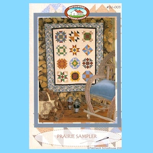 May include: A quilt pattern titled "Prairie Sampler" featuring a patchwork design with various geometric shapes and colors. The quilt is displayed on a wall in a rustic setting with a rocking chair and a basket of pine cones.