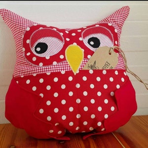 May include: Red and white polka dot owl pillow with a yellow beak and black eyes. The pillow has a gingham fabric on the back and a brown tag that says "Big Bird".