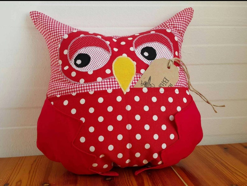May include: Red and white polka dot owl pillow with a yellow beak and black eyes. The pillow has a gingham fabric on the back and a brown tag that says "Big Bird".