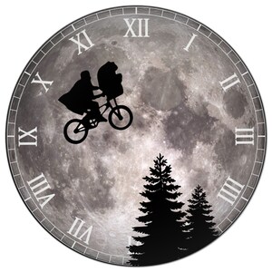 May include: A clock with a moon-like face featuring a silhouette of a bicycle with two figures riding on it. The clock face also has Roman numerals and two pine trees in the bottom right corner.