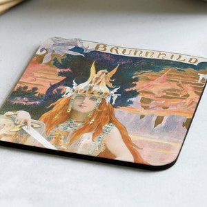 May include: A square coaster with a colorful illustration of a woman with red hair wearing a crown and holding a sword. The background is a landscape with mountains and trees. The text "BRUNNHILD" is printed in gold at the top of the coaster.