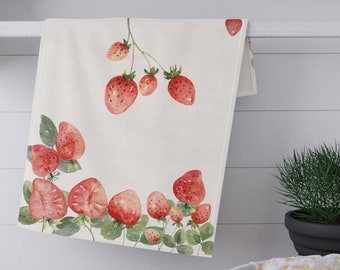 Puede incluir: Una toalla de cocina blanca con un diseño de acuarela de fresas rojas y hojas verdes. La toalla está colgada en un estante blanco con frascos de especias en el estante.