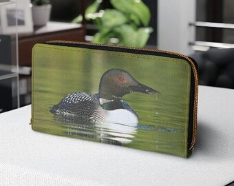 May include: A green zippered wallet with a photo of a loon swimming in a lake. The loon has black and white feathers and red eyes.
