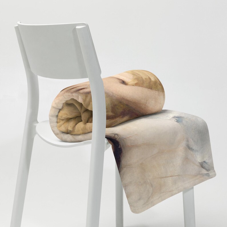 May include: A rolled-up blanket in shades of beige and brown sits on a white chair. The blanket has a soft, textured appearance, with a watercolor-like design. The chair is a simple, modern design.