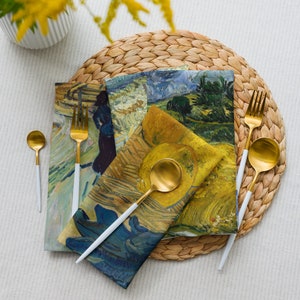 Può includere: Tre tovaglioli di stoffa con un sottopiatto in paglia intrecciata. I tovaglioli presentano una varietà di stampe artistiche astratte colorate. Due forchette dorate e un cucchiaio dorato sono posizionati sul sottopiatto.
