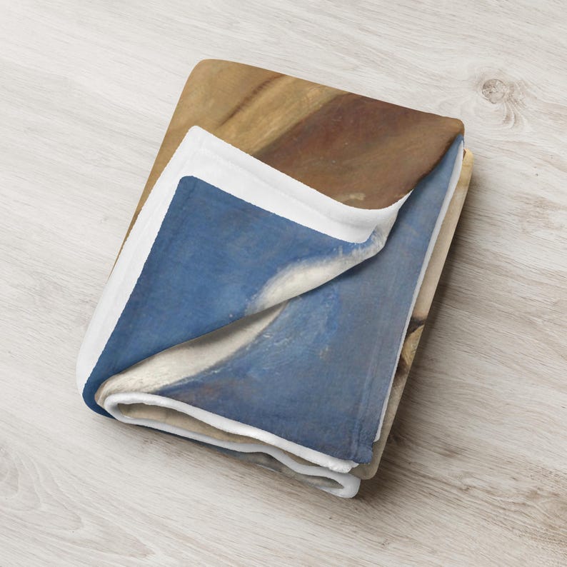 May include: Folded throw blanket in shades of brown and blue. The blanket has a white border and is folded, displaying the contrasting colours and textures of the fabric. The blanket is made of soft material.